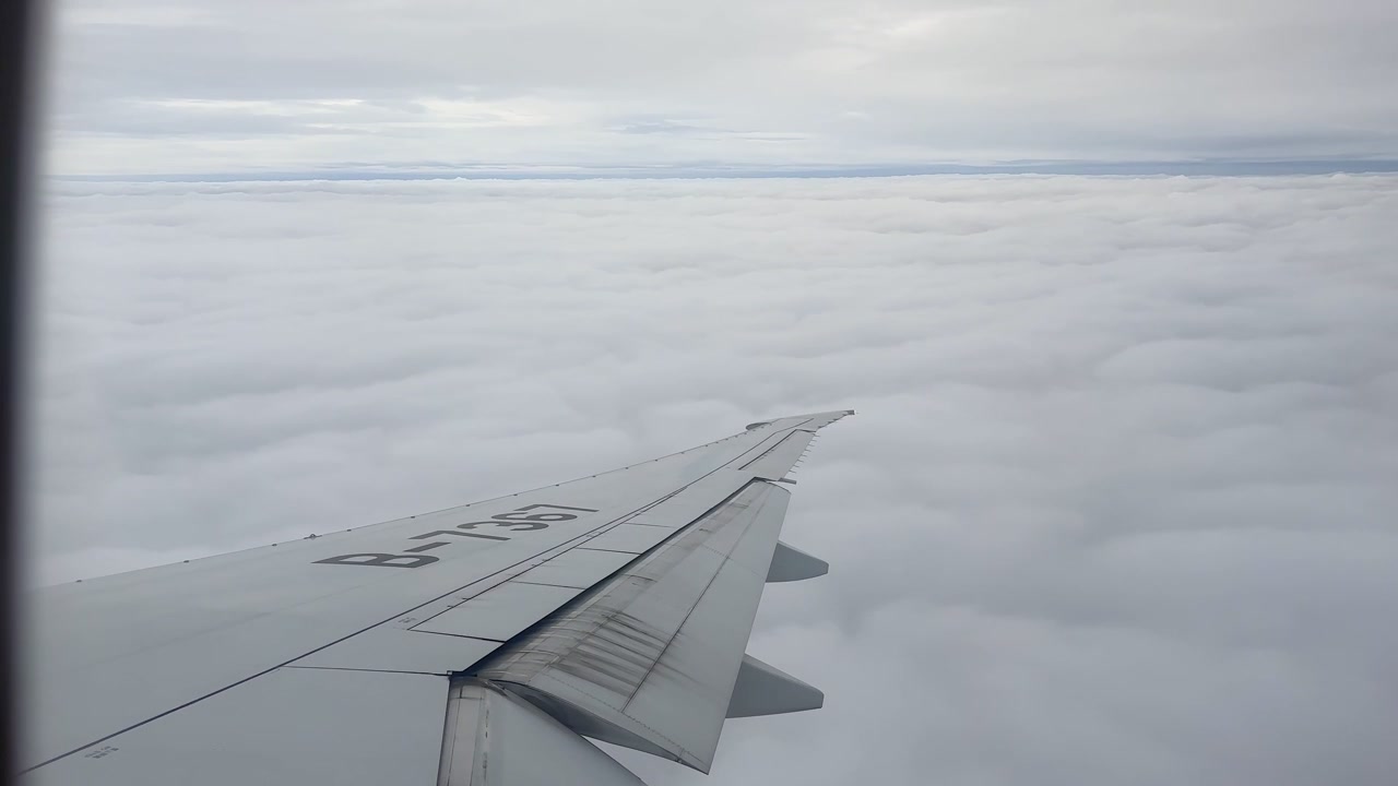 Udsigt fra et flyvindue, der viser vingen over et stort lag hvide skyer. Lys himmel strækker sig over horisonten under flyvning over Rusland