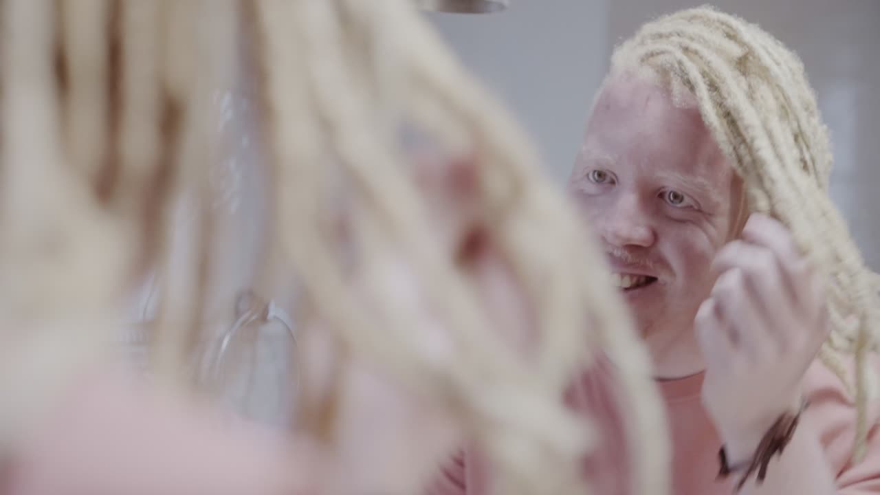 Albino man with dreadlocks grooming in front of a mirror