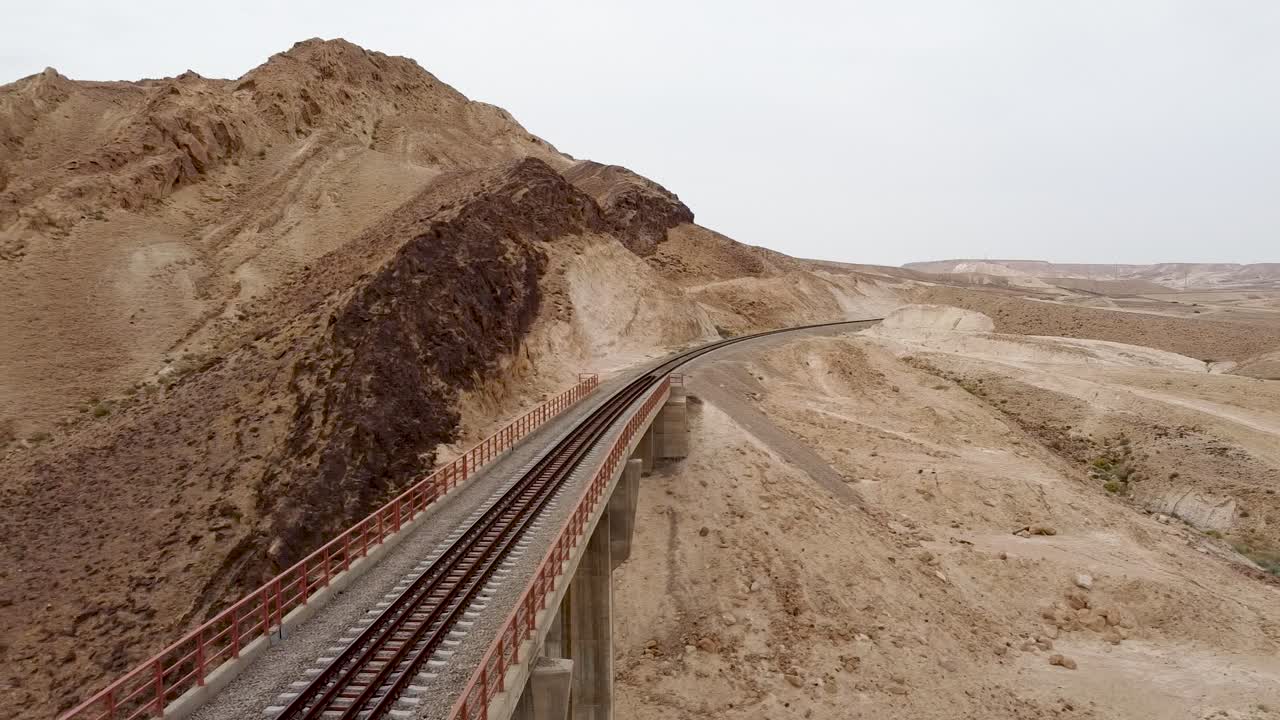 toma aérea de un dron de deslizamiento lento de un puente ferroviario de tren vacío, que revela una montaña y el desierto a la luz del día