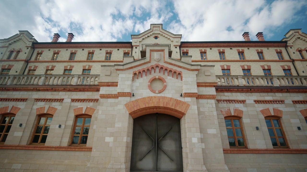 Široký čelní pohled na vinařský zámek v Moldavsku, s velkolepou historickou budovou, symetrickou fasádou, upravenými živými ploty, štěrkovou cestou a dramaticky modrou oblohou.