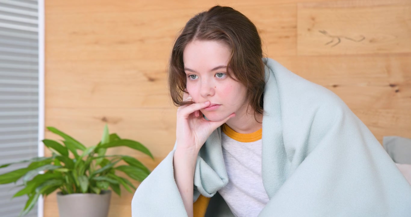 Adult female in blue blanket on sofa, camera zooming, straightening leaning to focus off-camera