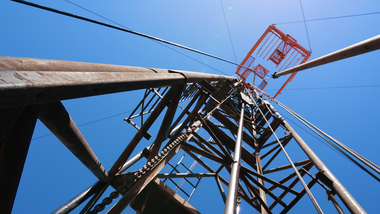 Standing at the foot of the derrick for drilling oil. Low angle view at the tower with boer producing oil.