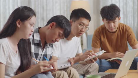 close up of asian teen group studying on a laptop at home. taking online course, a boy in plaid shirt hands up, asking question, giving an answer, writing into notebook