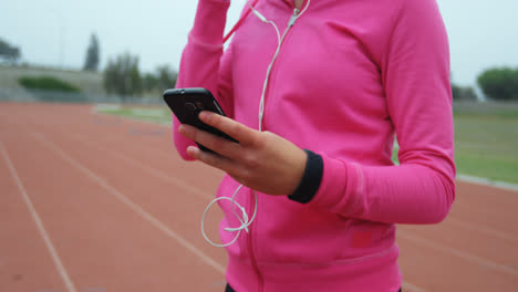 Mittelteil-Einer-Sportlerin,-Die-Auf-Einem-Sportplatz-Mit-Dem-Mobiltelefon-Musik-Hört,-4k