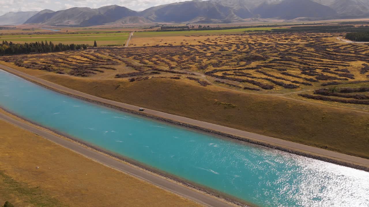 Car driving next to man-made hydro canal on New Zealand's south Island
