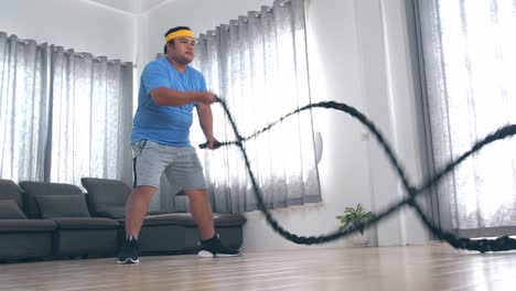 overweight asian man performing battle rope exercise at home