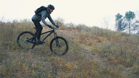 homem atleta com mochila e capacete andando de mountain bike descendo a colina