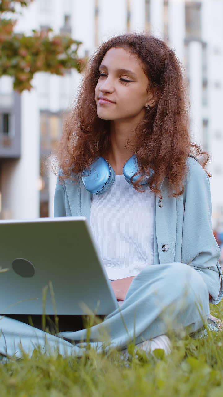 Bambina preadolescente freelancer che chiude il PC portatile dopo aver terminato il lavoro, seduta sull'erba in un parco cittadino