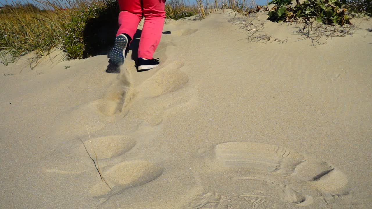 Kvinnen løper på sanddyner til havet. Sakte film.