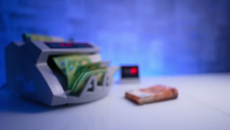 stack of green banknotes places to a cash counting machine. hand takes money and places near the fifty-euro bill pile. blurred image.