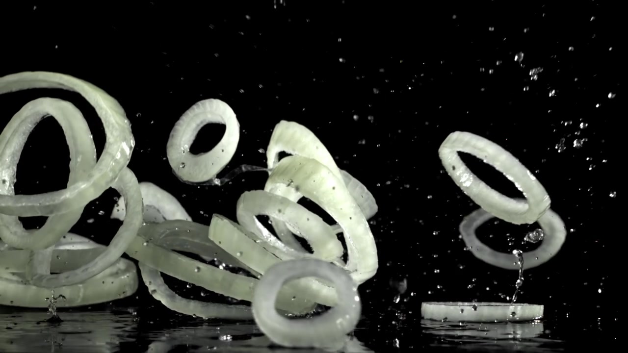 Sliced Onion Rings Falling and Splashing on a Wet Black Surface in Slow Motion
