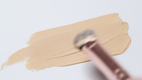 brushing a layer of make-up foundation on a clean, white palette board to check its texture and tone