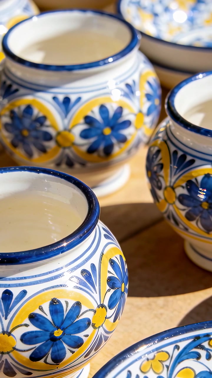 Video verticale: Vaso di ceramica mostrato mentre la telecamera si sposta verso destra sul tavolo, rivelando vasi blu-gialli.