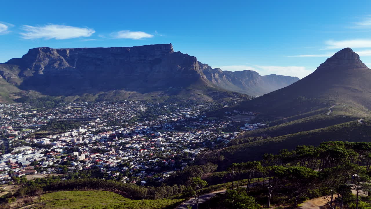 Cinematic aerial view of Table Mountain and Cape Town cityscape, showcasing rugged cliffs, urban sprawl, and South Africa’s iconic natural landmark under clear blue sky