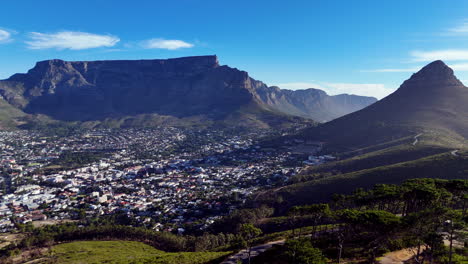 cinematic aerial view of table mountain and cape town cityscape, showcasing rugged cliffs, urban sprawl, and south africa’s iconic natural landmark under clear blue sky