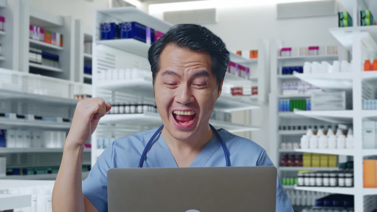 스테토스코프를 들고 노트북을 보고 약국에서 성공을 축하하는 아시아 남성 의사의 클로즈업