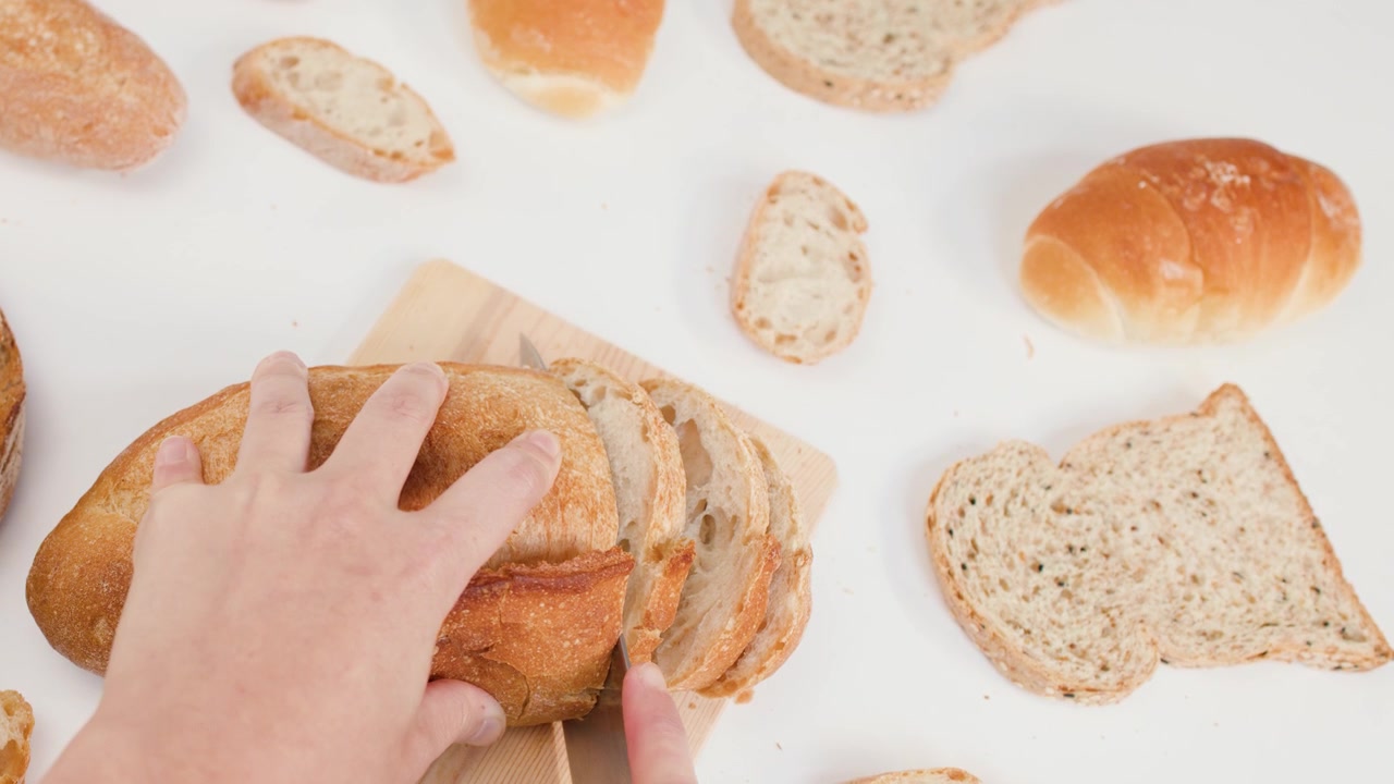 Overhead shot of hands using a knife to slice organic sourdough on white background.