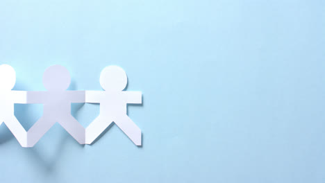 close up of people holding hands made of white paper on blue background with copy space