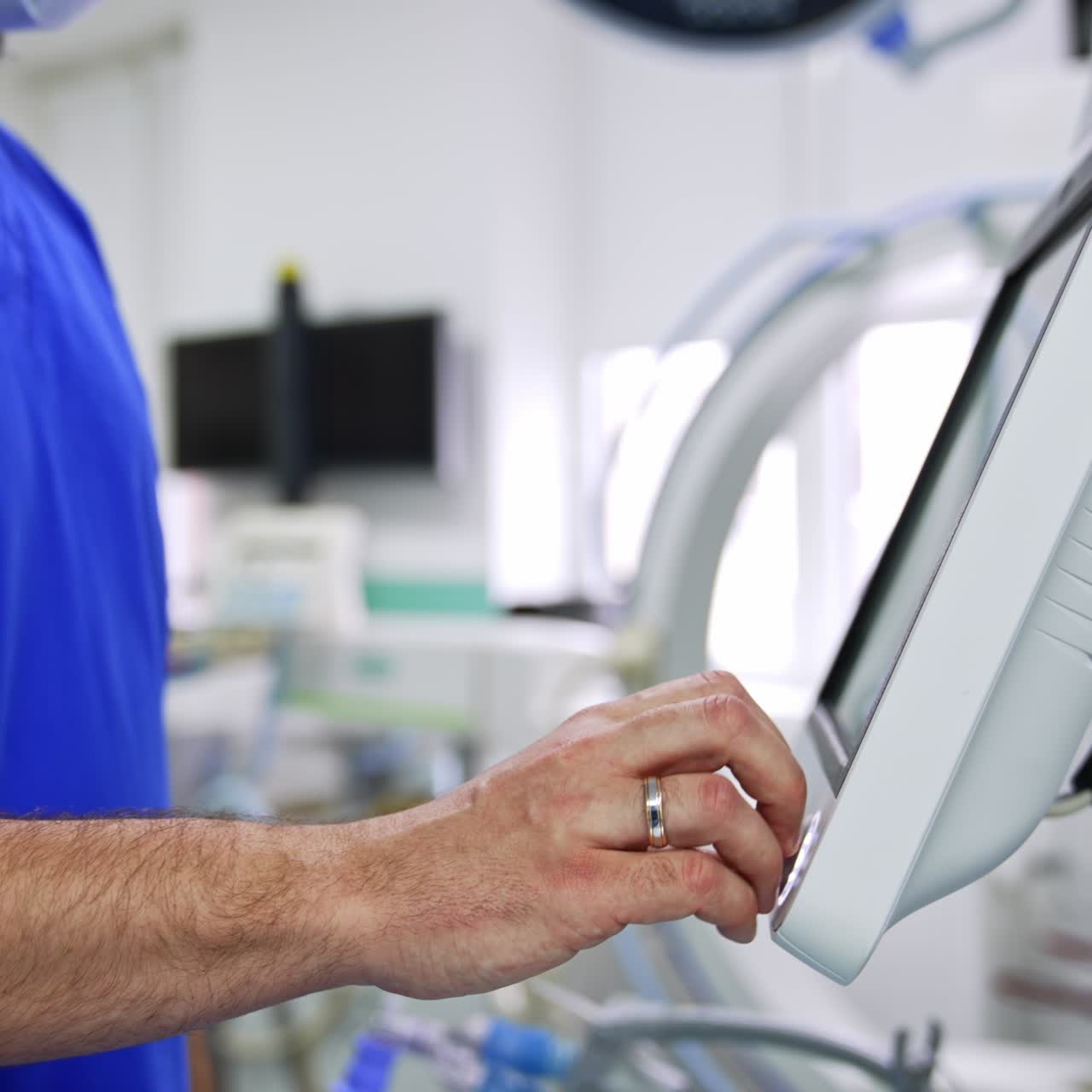 Unrecognized doctor switching on the equipment in modern surgical theatre. Specialist pressing the keys on the sensor screen. Side view