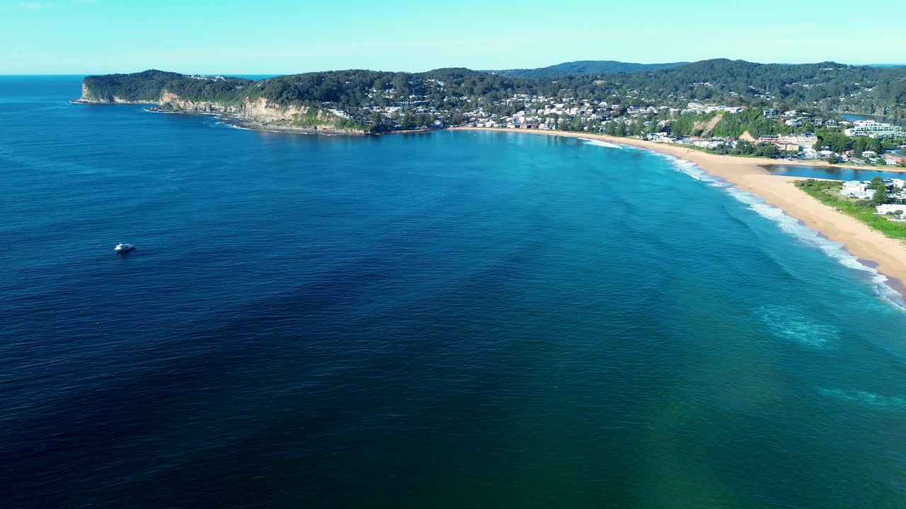 Drone aerial landscape of ocean waves swell with seaside coastal town in the background of Avoca Beach suburbs bushland coastline headland bay Central Coast Australia tourism travel nature outdoors
