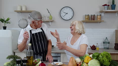 Glückliches-Seniorenpaar-Tanzt-Beim-Gemeinsamen-Kochen-In-Der-Küche-Mit-Frischem-Gemüse-Und-Obst