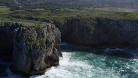 static aerial establishing of bufones de pria cavern in asturias spain as ocean waves crash on sharp rock, slow motion