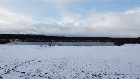 Aerial-through-forest-pathway-covered-in-snow-towards-the-lake-of-Lommelse-Sahara,-Winter-Landscape