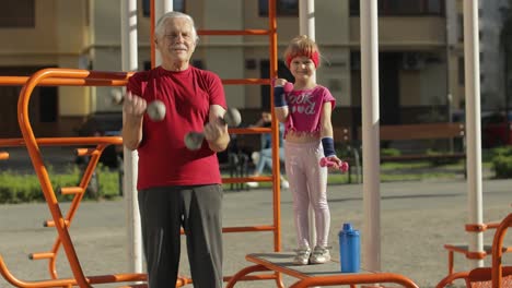 Granddaughter-and-grandfather-doing-fitness-exercises-with-dumbbells.-Senior-man-with-child-kid-girl