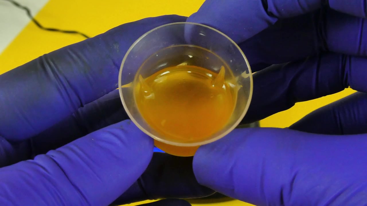 Tecnico di laboratorio che mescola un'emulsione cosmetica arancione in una piccola tazza con un agitatore magnetico.