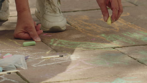 medium shot of the hands of a grandma drawing with an orange piece of chalk onto some stones outside