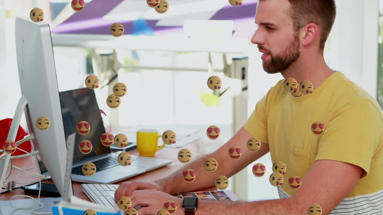 múltiples emojis de cara flotando contra el hombre usando la computadora en la oficina