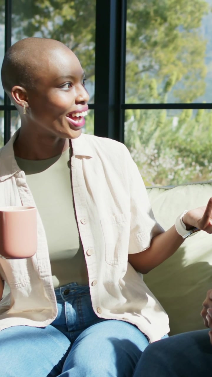 Vertical video: Holding pink mug with partner speaking, woman gesturing and explaining on couch