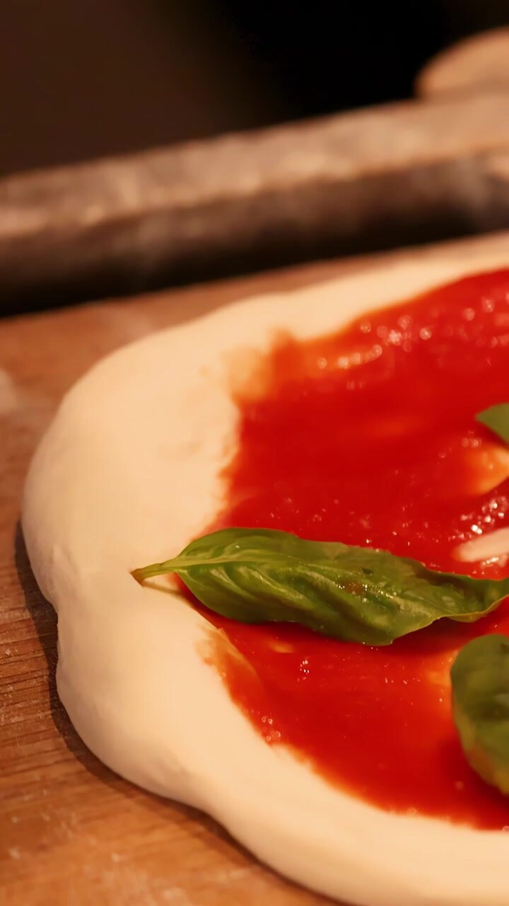 Primo piano di mani che aggiungono basilico all'impasto crudo della pizza in una cucina professionale