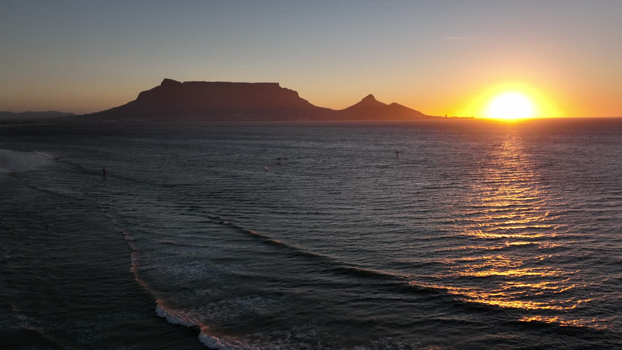 Cape Town South Africa windsurfers sailing windy surf wave Table Mountain drone aerial cinematic Lions Head sunset beach stunning mountain and ocean landscape orange gold sun on horizon backward pan