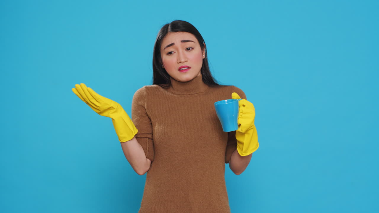 Pensive thoughtful maid holding cup of coffee standing over blue background in studio
