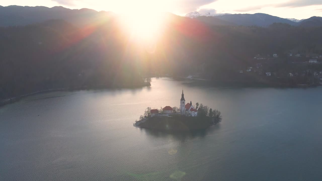 Aerial view of chapel on small island in middle of beautiful lake surrounded by huge mountains. Birds eye view.