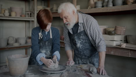 senior potter teaching a young student in a pottery studio