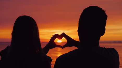 silhouettes of a young couple hands show the shape of the heart against the backdrop of the sunset o