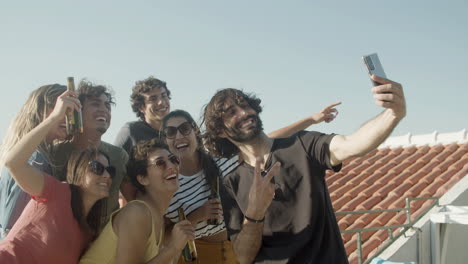 happy bearded man taking a selfie photo with friends who holding beer bottles during a rooftop party