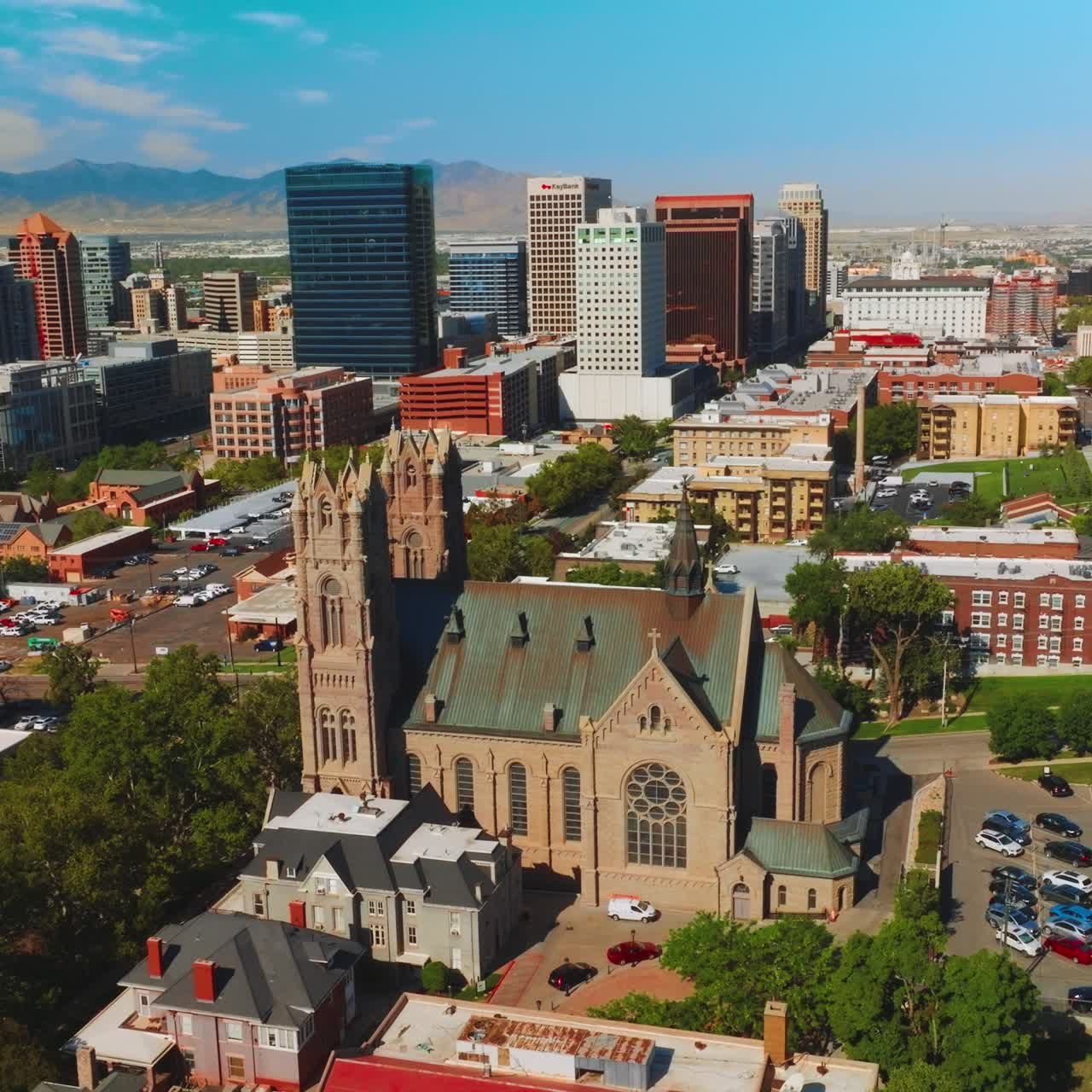 Historic building of a Cathedral of Madeleine locating among the modern architecture. Salt Lake City panorama at backdrop of Utah mountains on sunny day