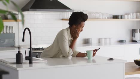 Feliz-Mujer-Afroamericana-Tomando-Café-Y-Hablando-Por-Teléfono-Inteligente-En-La-Cocina