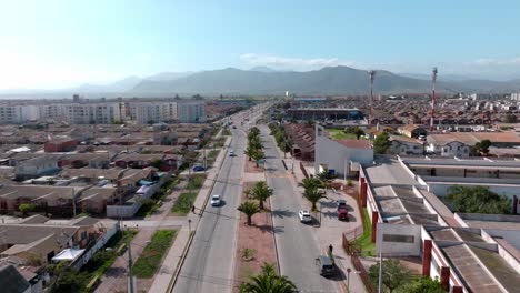 dolly in aerial view of a road with small palm trees in the center and an illuminated mountain on a sunny day on the horizon, la serena, chile