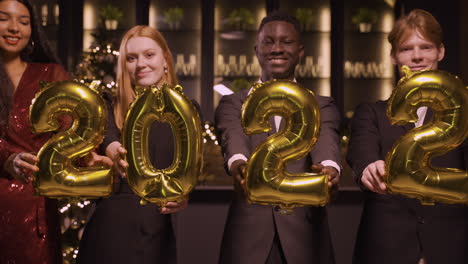 grupo de amigos con ropa elegante sosteniendo globos con los números 2022 mientras bailan en la fiesta de año nuevo 1