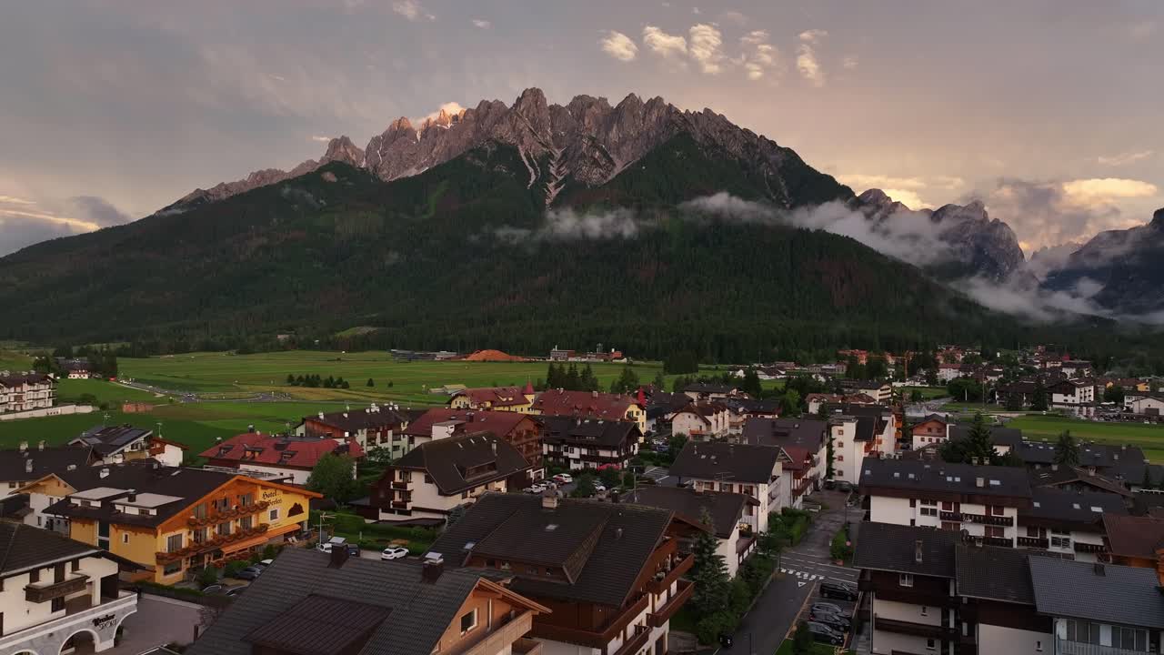 Aerial establishing overview of Toblach city with fields and mountain landscapes, showing quaint rural area as mist descends valley