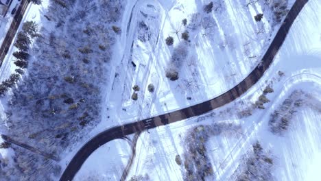 aerial zoom in survey over snow covered curvy highway freeway inbetween a park with light traffic on beautiful winter day overlooking a frozen residential area by the road 2-2