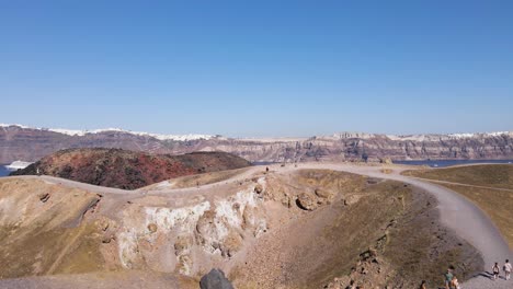 Aerial-view,-passing-by-a-man-in-front-of-volcano-crater-in-Santorini-island,-Greece-in-slow-motion