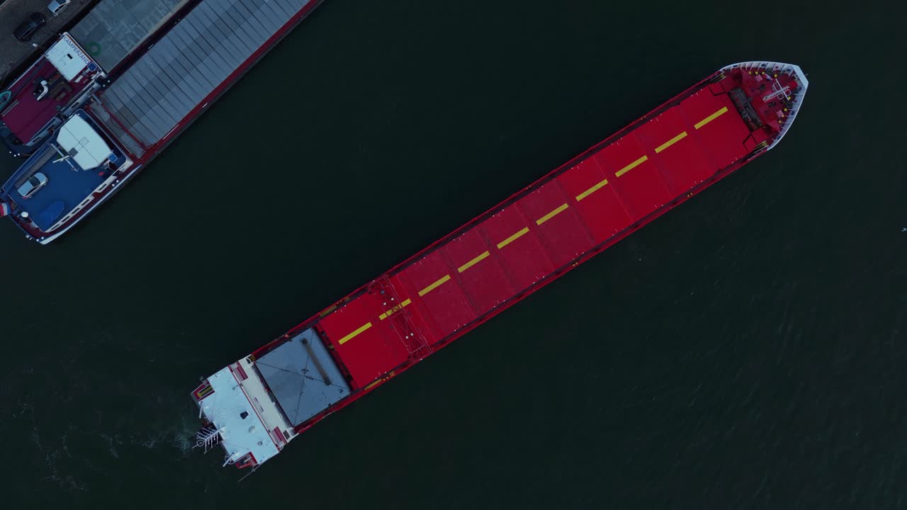 Eems River cargo ship ready to navigate on Oude Maas distributary beside industrial platform from above, Dordrecht, Zuid-Holland, Netherlands
