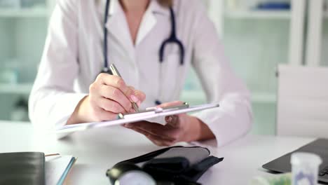 close-up of a doctor writing on a clipboard in a medical setting