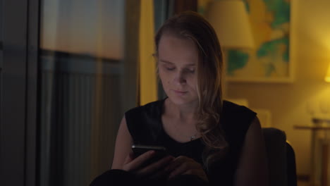 mujer con un teléfono inteligente en el interior acogedor de la noche