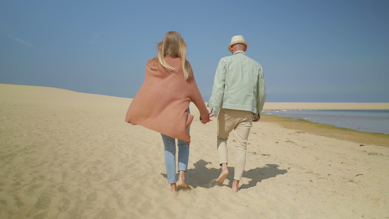una pareja feliz caminando por la playa de arena.